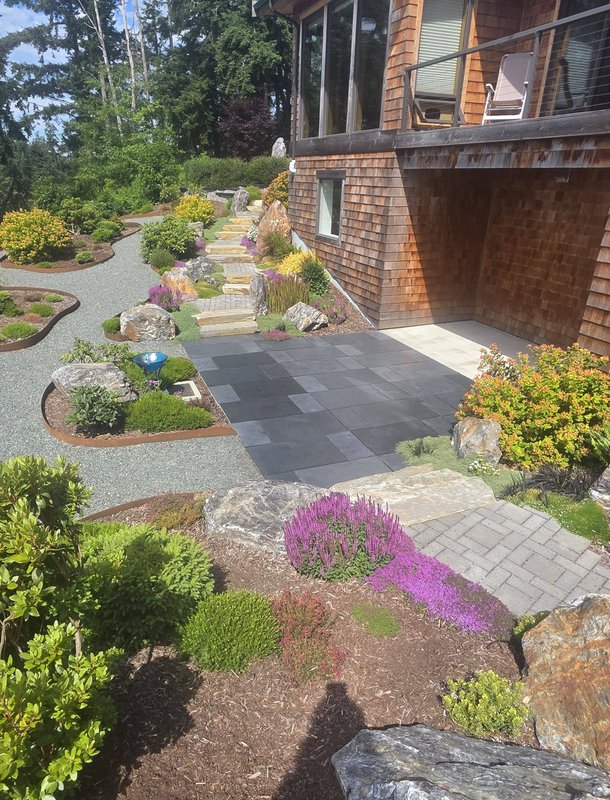 Rock garden, gravel path, and stone patio beside a cedar-shingle house