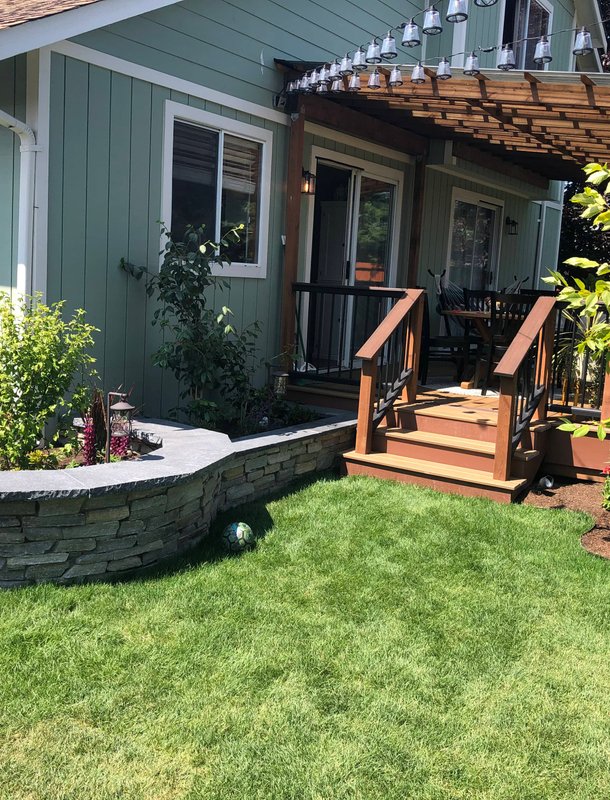 Backyard lawn with a curved stone planter and pergola deck in Oak Harbor